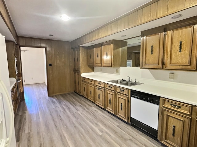 kitchen with white dishwasher, light hardwood / wood-style floors, wood walls, and sink