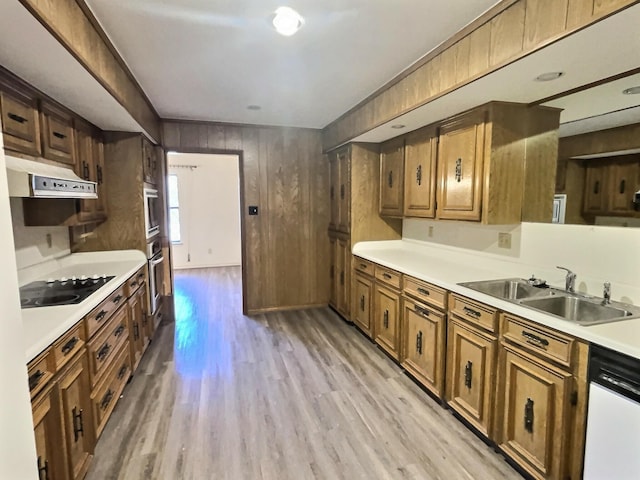 kitchen with sink, dishwasher, light hardwood / wood-style floors, wood walls, and black electric cooktop