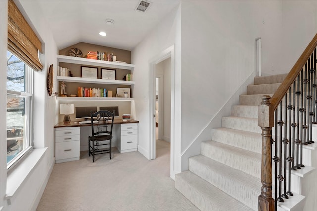 staircase with a wealth of natural light, built in features, built in desk, and carpet flooring