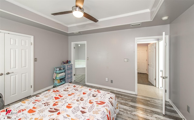 bedroom featuring hardwood / wood-style floors, ceiling fan, a closet, a tray ceiling, and crown molding