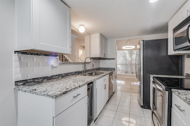 kitchen with stainless steel appliances, sink, white cabinets, light tile patterned flooring, and tasteful backsplash