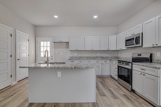 kitchen featuring a center island with sink, appliances with stainless steel finishes, light stone countertops, sink, and white cabinetry