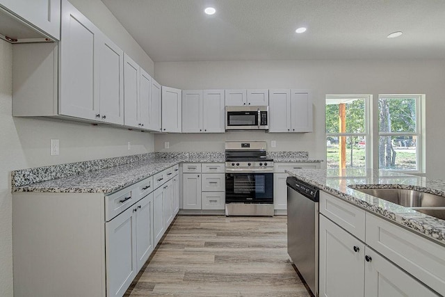 kitchen featuring white cabinets, light hardwood / wood-style flooring, light stone counters, and appliances with stainless steel finishes