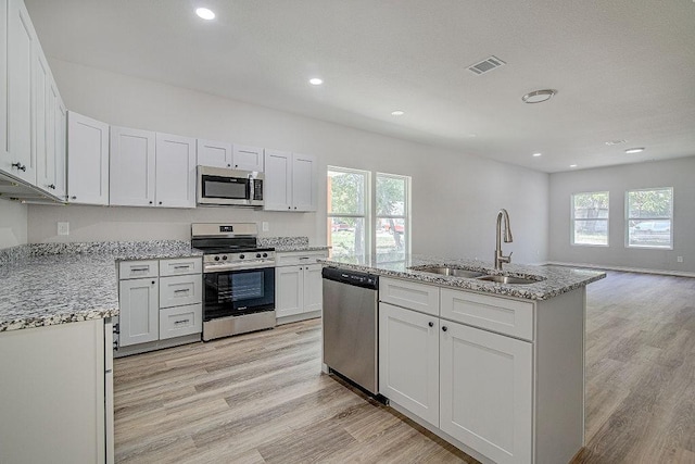 kitchen featuring stainless steel appliances, sink, white cabinets, light hardwood / wood-style floors, and a center island with sink