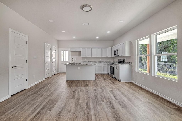 kitchen featuring light stone counters, stainless steel appliances, an island with sink, light hardwood / wood-style floors, and white cabinets