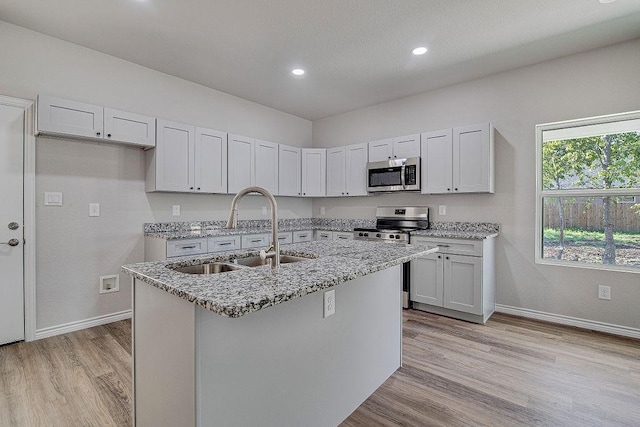 kitchen with appliances with stainless steel finishes, white cabinetry, light stone counters, and sink