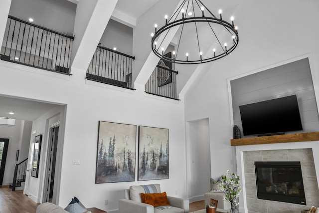 living room featuring a high ceiling, hardwood / wood-style flooring, a tiled fireplace, and a notable chandelier