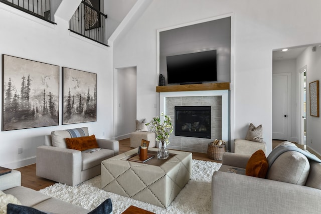 living room featuring a towering ceiling, wood-type flooring, and a tile fireplace