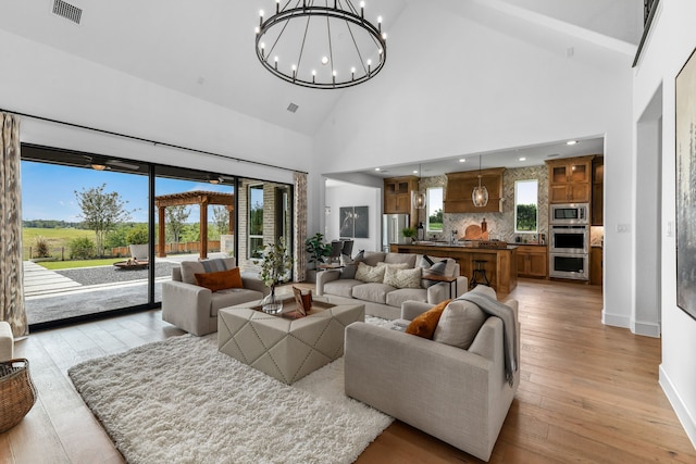 living room with high vaulted ceiling, an inviting chandelier, and light hardwood / wood-style floors