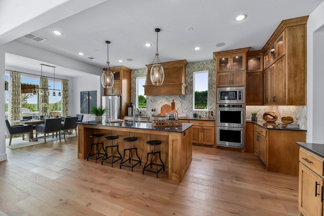 kitchen with stainless steel appliances, custom range hood, light wood-type flooring, and pendant lighting