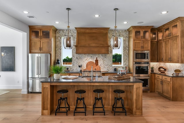 kitchen featuring appliances with stainless steel finishes, a kitchen breakfast bar, decorative light fixtures, and a center island with sink