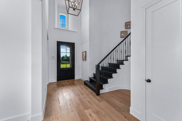 entryway with a towering ceiling, a notable chandelier, and light hardwood / wood-style flooring