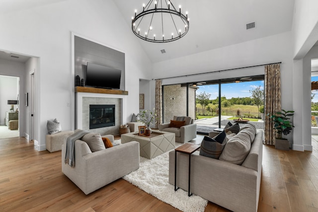 living room with a notable chandelier, hardwood / wood-style floors, high vaulted ceiling, and a fireplace