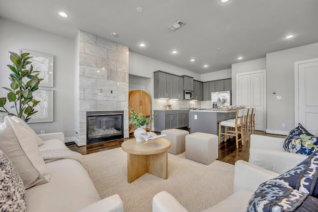 living room with a tile fireplace and dark wood-type flooring