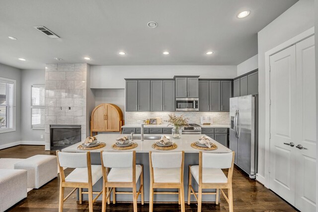 kitchen featuring appliances with stainless steel finishes, a tiled fireplace, an island with sink, a breakfast bar, and sink