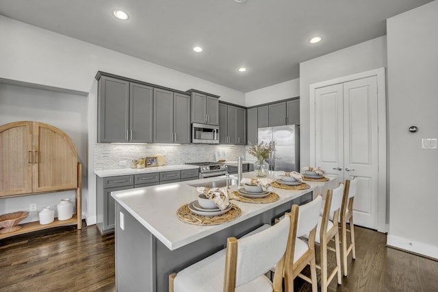 kitchen with stainless steel appliances, sink, gray cabinetry, and an island with sink