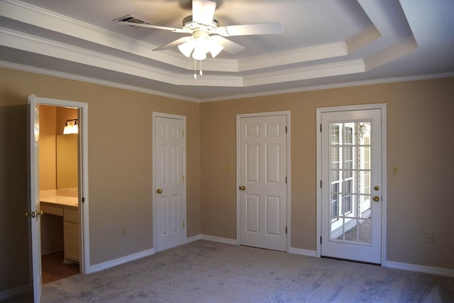 unfurnished bedroom featuring a raised ceiling, connected bathroom, light colored carpet, crown molding, and ceiling fan