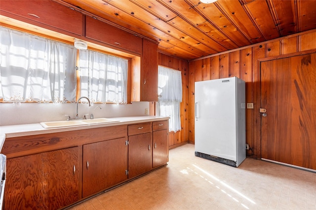 kitchen featuring sink, wood ceiling, white fridge, and wood walls