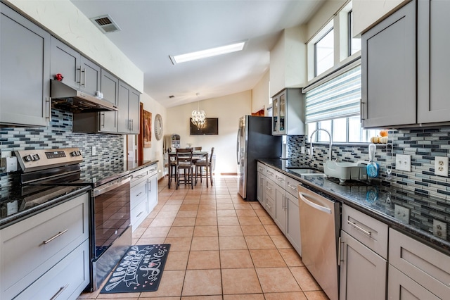 kitchen with gray cabinetry, stainless steel appliances, light tile patterned floors, pendant lighting, and lofted ceiling