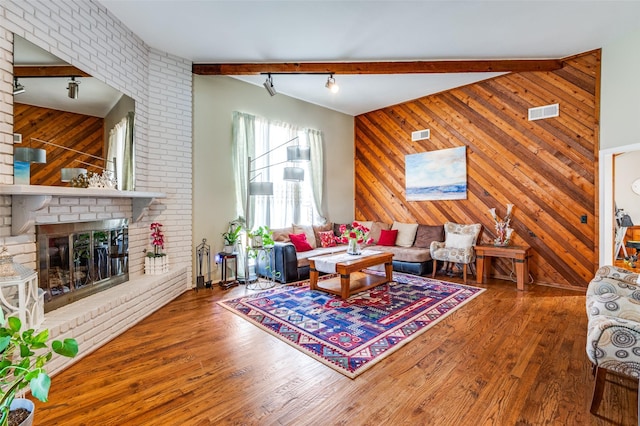 living room featuring wood-type flooring, wooden walls, beamed ceiling, and a fireplace