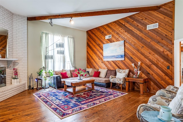 living room with wood-type flooring, wooden walls, a fireplace, and beamed ceiling