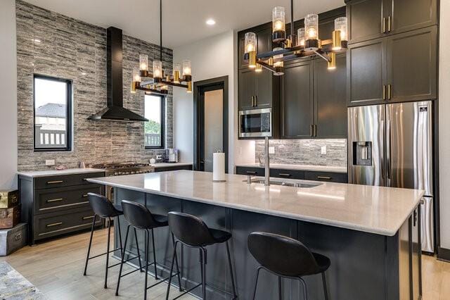 kitchen with sink, stainless steel appliances, wall chimney exhaust hood, and hanging light fixtures