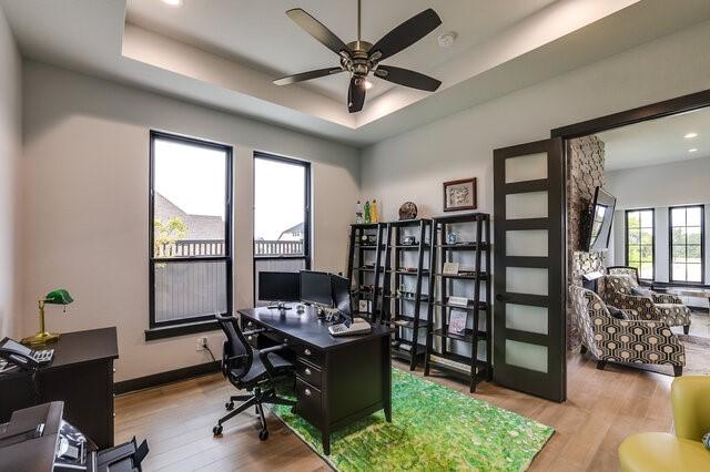 office space with ceiling fan, a tray ceiling, and light hardwood / wood-style flooring