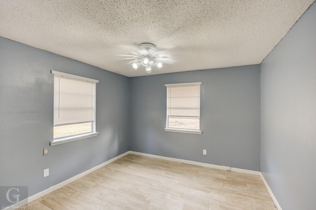 spare room featuring a textured ceiling, light wood-type flooring, and a healthy amount of sunlight