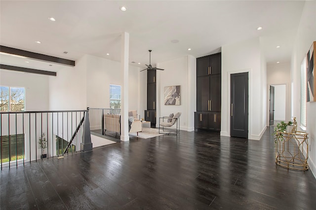 living room with ceiling fan, beamed ceiling, and dark wood-type flooring