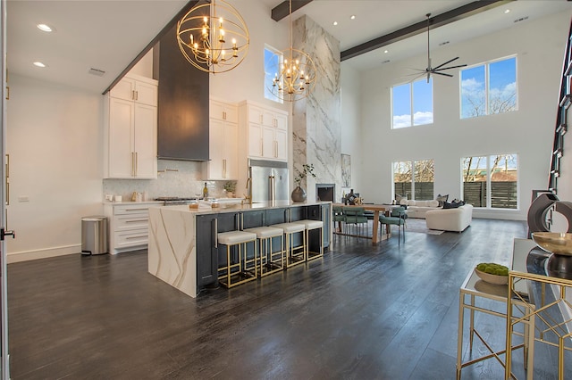 kitchen with a kitchen breakfast bar, a kitchen island with sink, dark hardwood / wood-style floors, beam ceiling, and white cabinets