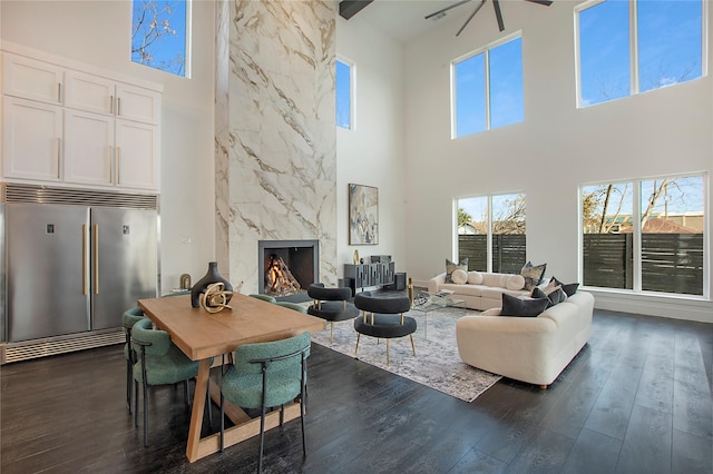 living room featuring ceiling fan, dark hardwood / wood-style flooring, a towering ceiling, and a fireplace