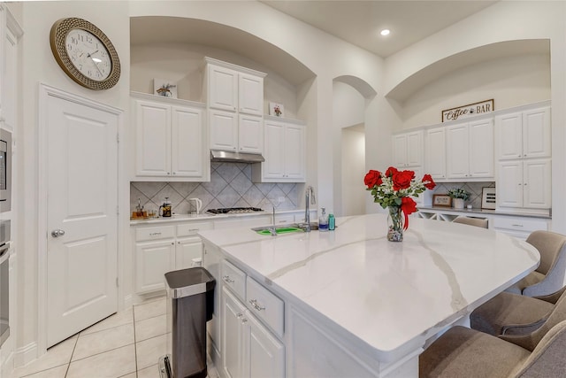 kitchen with sink, white cabinetry, light tile patterned floors, and an island with sink