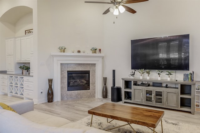 living room featuring a tiled fireplace, ceiling fan, and light wood-type flooring