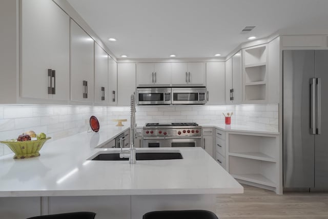 kitchen featuring premium appliances, kitchen peninsula, backsplash, white cabinets, and a breakfast bar