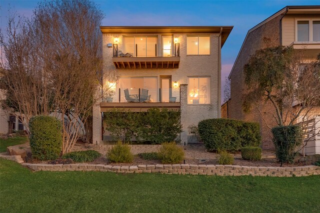 back house at dusk with a balcony and a lawn