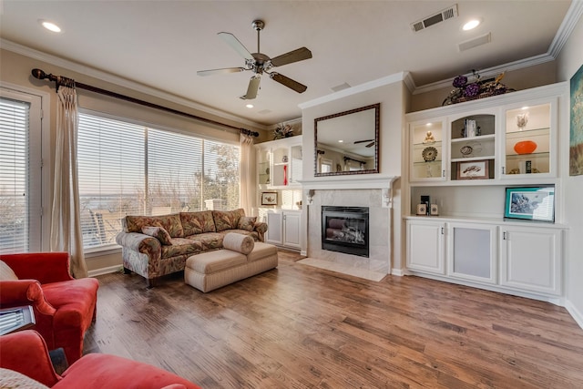 living room featuring crown molding, a premium fireplace, visible vents, and light wood-style floors