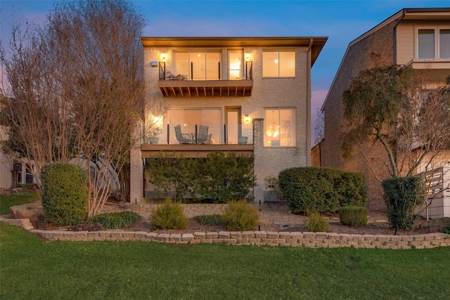 back of house at dusk with a yard and a balcony