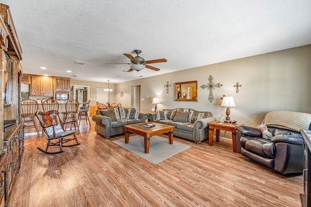 living room with a textured ceiling, ceiling fan, and light hardwood / wood-style flooring