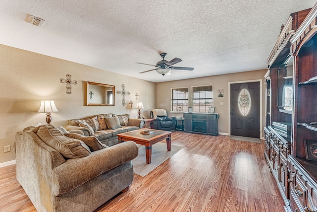 living room with a textured ceiling, light wood-type flooring, and ceiling fan