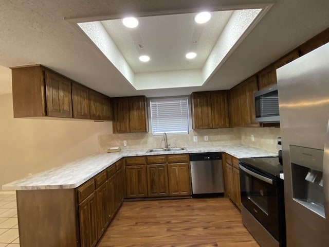 kitchen featuring stainless steel appliances, a raised ceiling, light wood-type flooring, backsplash, and sink