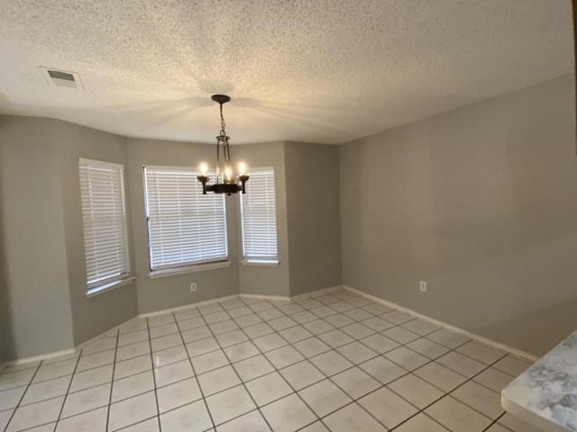 spare room with a textured ceiling, a chandelier, and light tile patterned floors