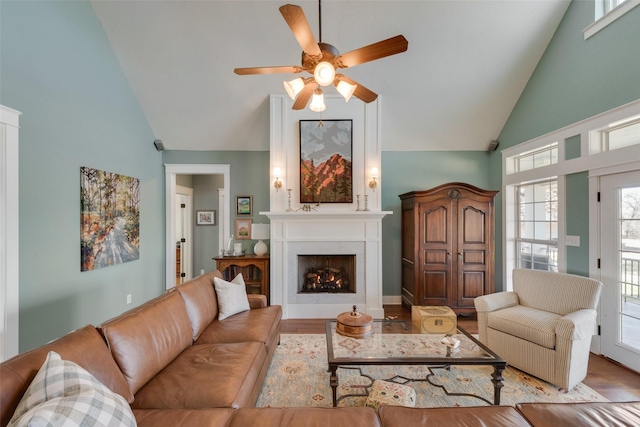 living room featuring a large fireplace, ceiling fan, light hardwood / wood-style flooring, and high vaulted ceiling