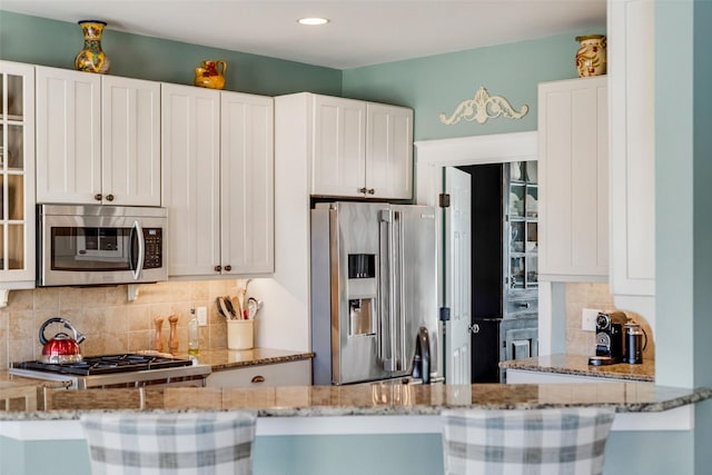 kitchen with appliances with stainless steel finishes, white cabinets, light stone counters, and decorative backsplash