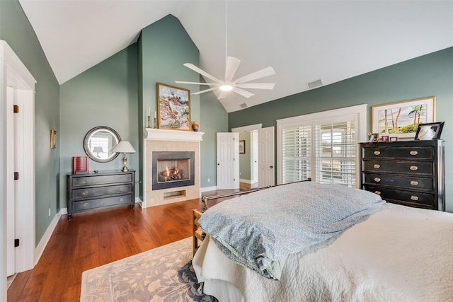 bedroom featuring high vaulted ceiling, a tiled fireplace, ceiling fan, and dark wood-type flooring