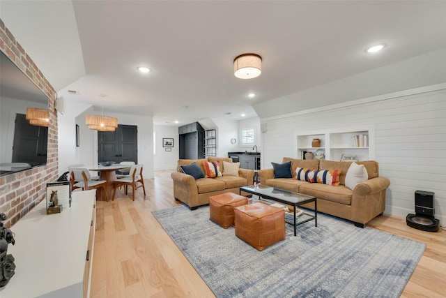 living room with lofted ceiling, wooden walls, light wood-type flooring, and built in shelves