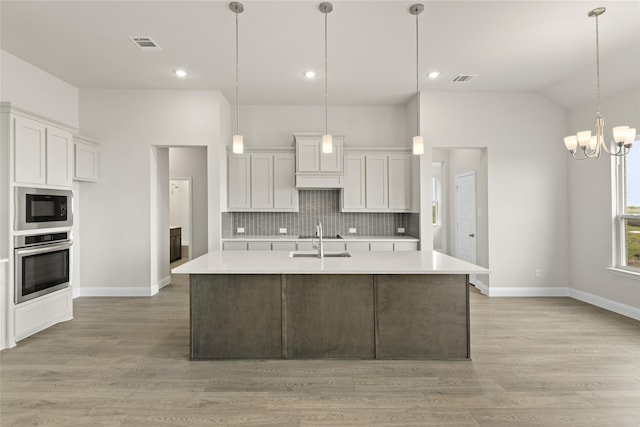 kitchen with oven, white cabinets, built in microwave, and an island with sink