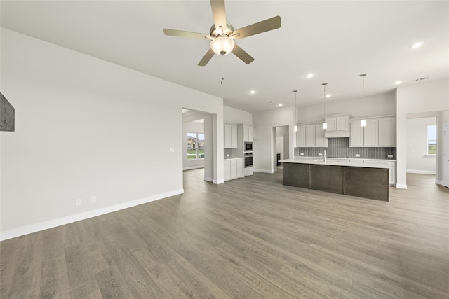 kitchen featuring pendant lighting, a kitchen island with sink, backsplash, hardwood / wood-style floors, and white cabinets