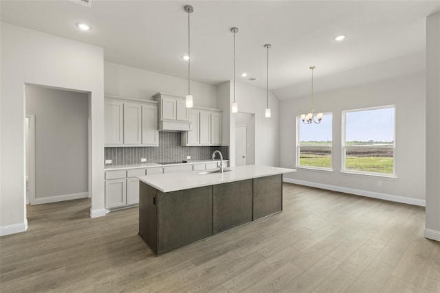 kitchen featuring hanging light fixtures, a center island with sink, tasteful backsplash, an inviting chandelier, and sink