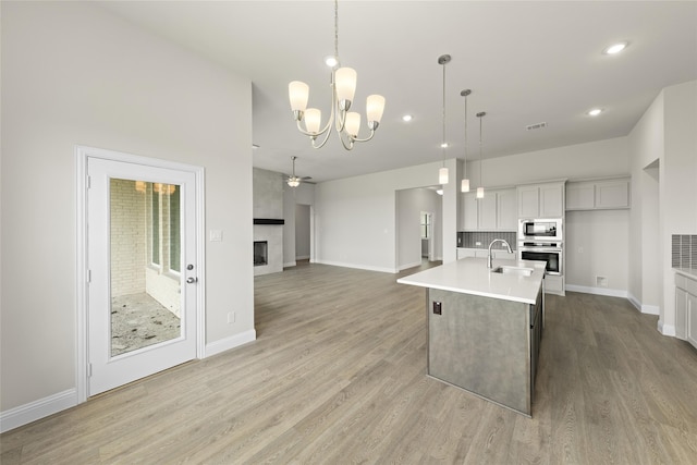 kitchen with sink, ceiling fan with notable chandelier, hanging light fixtures, a kitchen island with sink, and appliances with stainless steel finishes