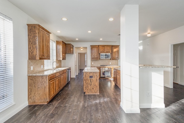 kitchen with dark wood-type flooring, sink, light stone counters, a kitchen island, and stainless steel appliances